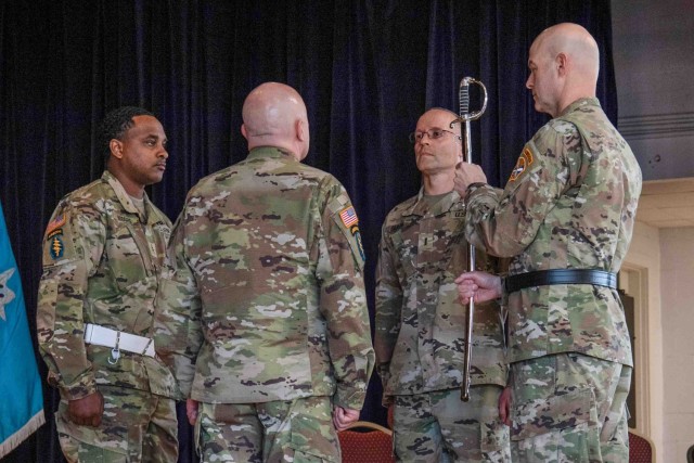Brig. Gen. Rhett R. Cox, right, the commanding general of Army Counterintelligence Command, holds the ceremonial sword alongside outgoing Command Chief Warrant Officer Aaron Skiles (second from right), incoming Command Chief Warrant Officer Jamie...