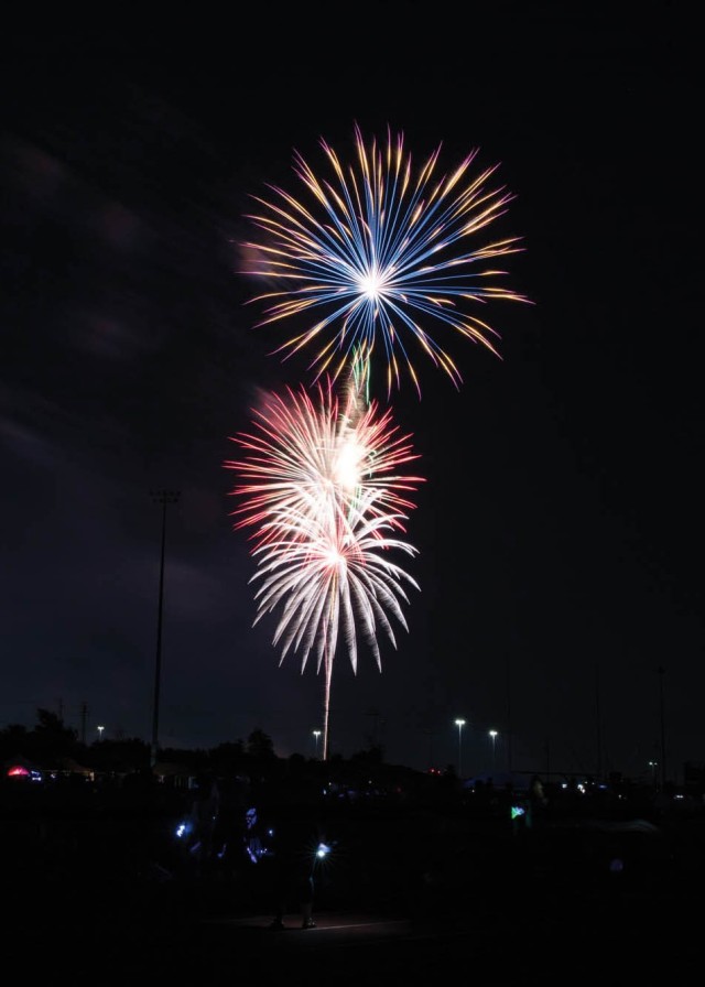 Fireworks explode in night sky, mixing colors of blue, red, white and yellow.