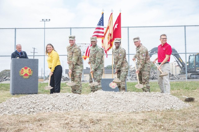 A group of people pose for a picture behind a mound a gravel while standing and holding shovels holding gravel.