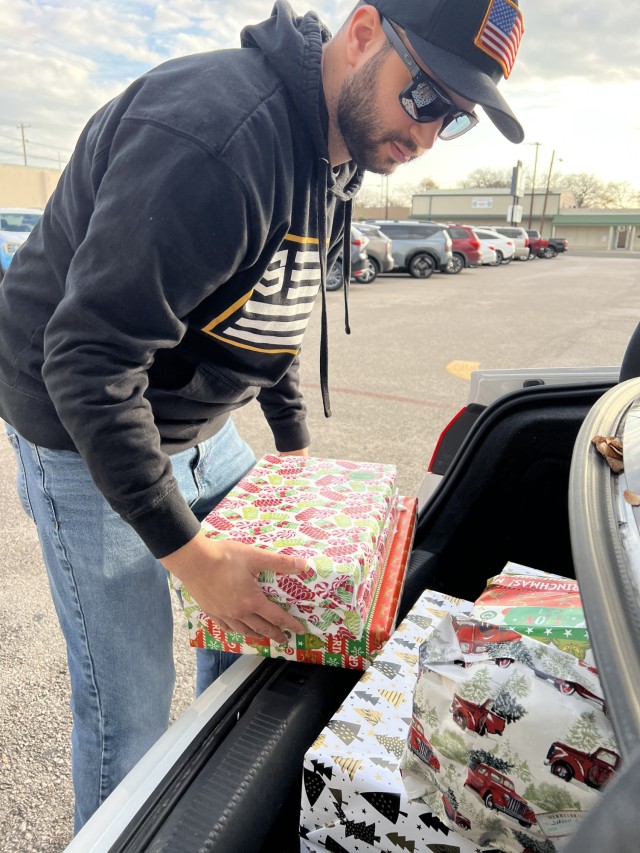 A man holds wrapped, rectangular boxes while in front of the trunk of a vehicle. 