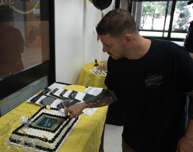 Chris Schiavi, manager of Infamous Ink, cuts the cake for the grand opening ceremony of a brand new tattoo parlor, at Fort Stewart, Georgia, Jan. 31. The tattoo parlor improves soldier morale and offers affordable solutions. (U.S. Army photo by...