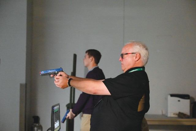 A man standing holds a handgun in front of him in both hands, arms outstretched.