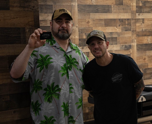 Chris Schiavi, owner of Infamous Ink, right, presents a $100 gift card to Jason Beheret, from Queens, New York, at Fort Stewart, Georgia, Jan. 31. Infamous Ink is the first-ever tattoo shop located on base. (U.S. Army photo by Pfc. Henry Benson)