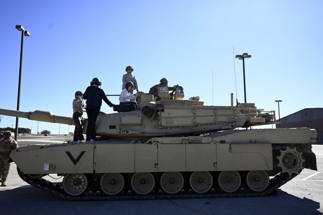 People stand and sit atop a military vehicle wearing helmets as they look around.