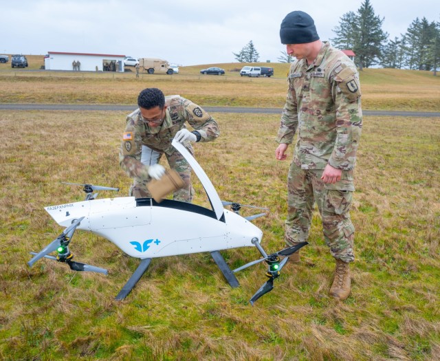 Sgt. 1st Class Kenneth Day retrieves simulated blood supplies delivered by a blueflite drone while Sgt. Benjamin Keikkala provides security during a field training exercise at Camp Rilea, Oregon, Jan. 30, 2025. The innovative drone delivery system demonstrated rapid resupply capabilities for combat medics in tactical environments. (U.S. Army National Guard photo by Maj. W. Chris Clyne, Oregon National Guard Public Affairs)