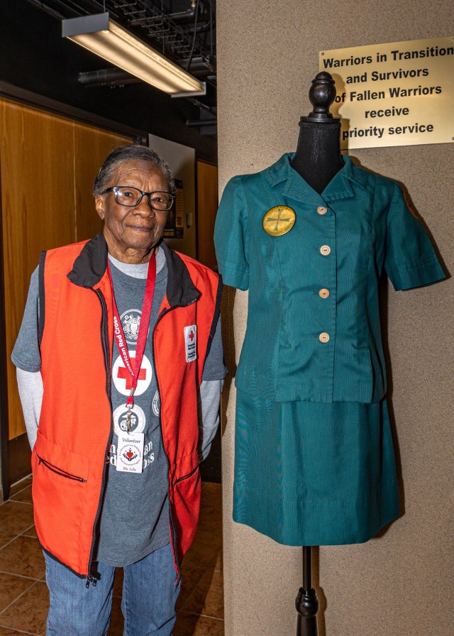 Lela Williams, donning her current Red Cross volunteer uniform, stands with her 1970s Army Community Service volunteer uniform at Fort Knox, Kentucky, Feb. 12, 2025. Williams has been a volunteer with the installation for over 50 years through ACS...