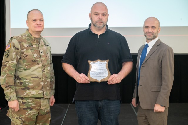 Three people pose for a photo during the presentation of Tobyhanna Army Depot's Supervisor of the Quarter award. The recipient, at center, holds a plaque.