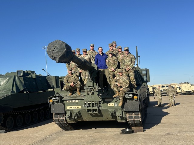 A group of people stand close together atop a military vehicle smiling.