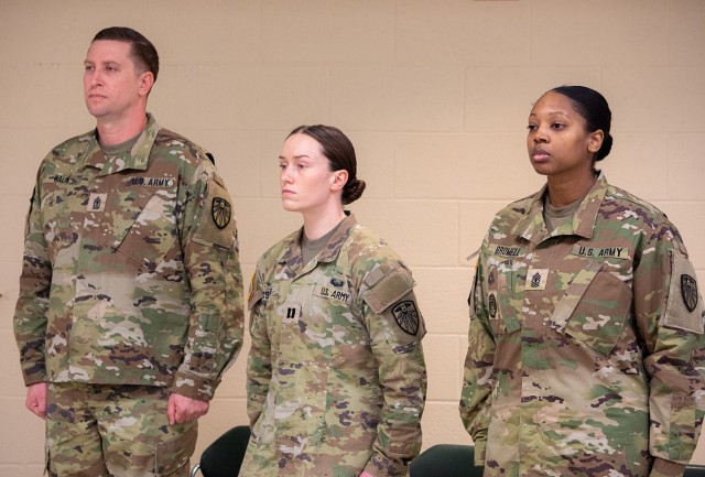 Outgoing 7th Signal Command (Theater) HHC First Sgt. David Walik, HHC Commander Cpt. Sophie Rosado, and incoming First Sgt. Candice Bromell, stand at attention during the ceremony.