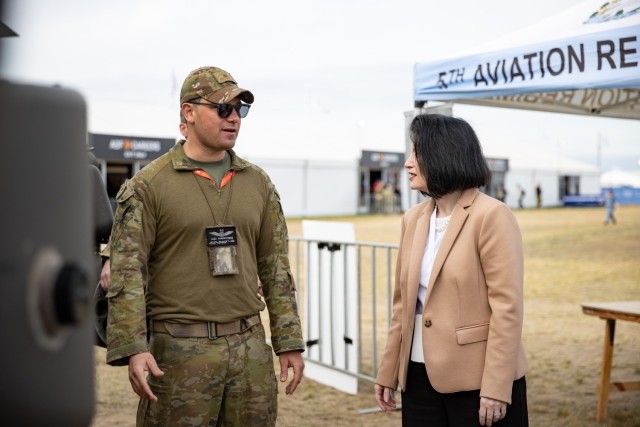 Australian Army Capt. Alex Paranthoine, an AH-64E Apache helicopter exchange pilot assigned to 16th Combat Aviation Brigade, explains the AH-64E’s key features and capabilities to Ms. Mary Beth Morgan, deputy director of the Defense Security...