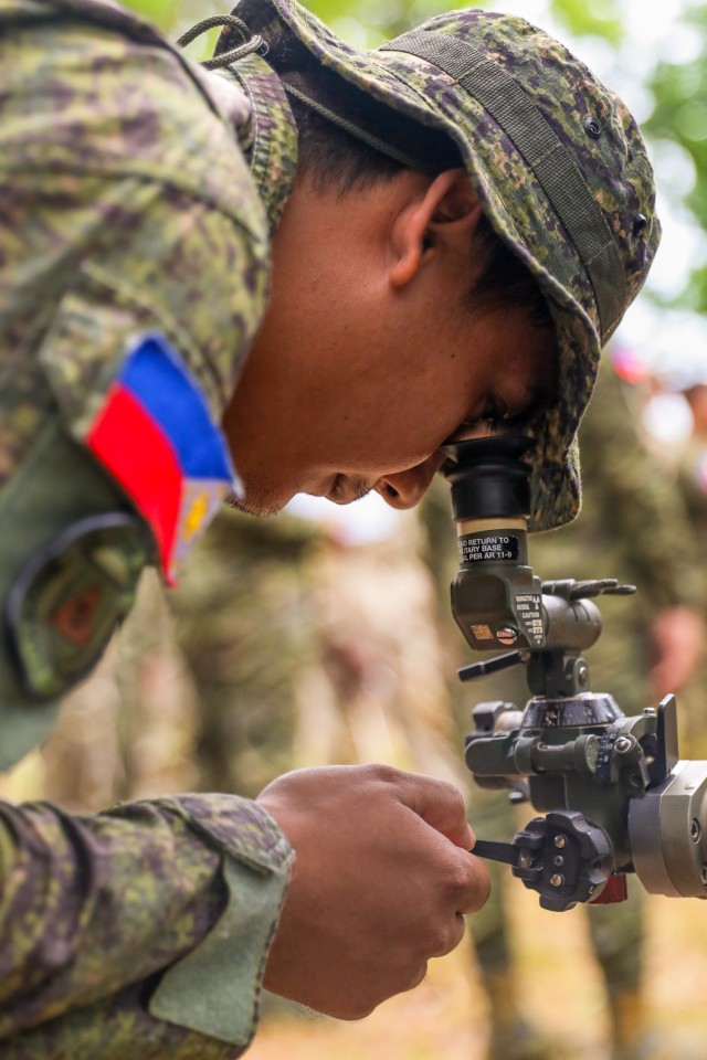 A soldier of the Philippine Army peers down the sight of a M252 81mm mortar firing system as part of a subject matter expert exchange on mortar operations training using the M252 18mm, M120, and 60mm mortar firing systems with U.S. Army Soldiers...