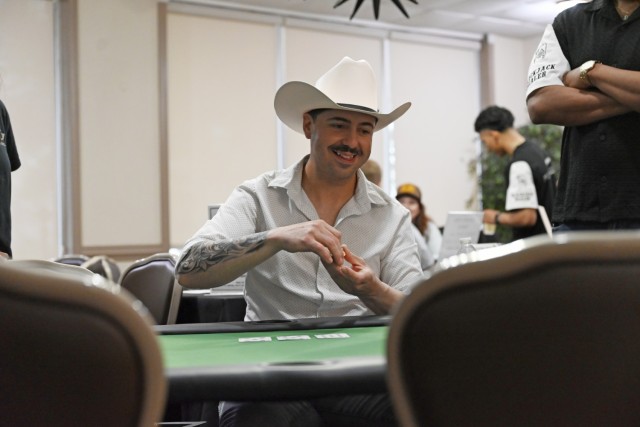 A man holds poker chips in his hands while looking down at a poker table he is seated behind.