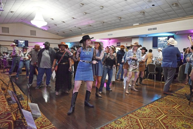 People stand in rows on a wooden dance floor, leaning to the left.