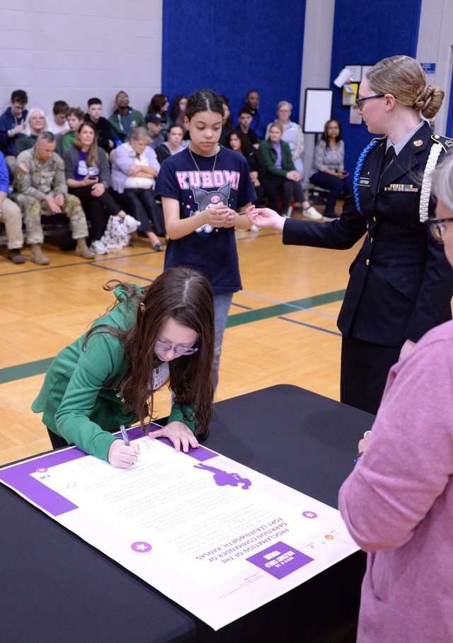 Representing the youth served by Osage School-Age Center, fourth-grader Olivia Drouin adds her signature to the Month of the Military Child proclamation, followed by fifth-grader Saraphim Isbell and Leavenworth High School JROTC cadet Alexis...