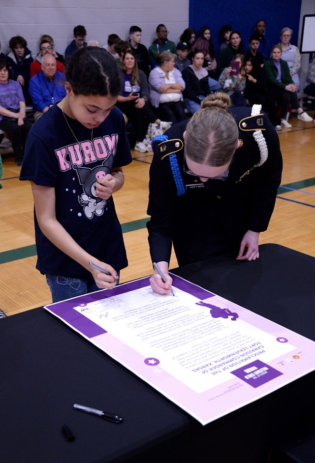 Fifth-grader Saraphim Isbell, representing the youth served by Osage School-Age Center, and Leavenworth High School JROTC cadet Alexis Hoffman, representing the youth served by Harrold Youth Center, add their signatures to the Month of the...