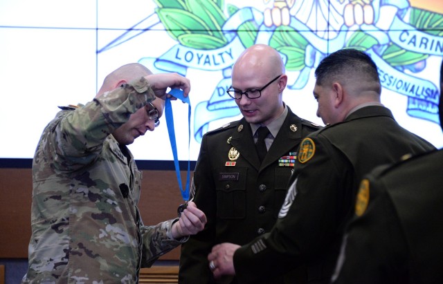 Master Sgt. Vincent Jarman, Army Corrections Brigade, left, and Sergeant Audie Murphy Club Lamp Chapter President 1st Sgt. Martin Alonzo, ACB, right, help untwist the SAMC medallion for Staff Sgt. Quinlan Simpson, C Company, U.S. Disciplinary...