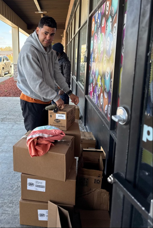 A man stands next to several cardboard boxes sitting next to a building wall.