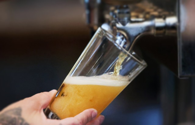 A hand is holding a glass as beer is filling it from a tap.