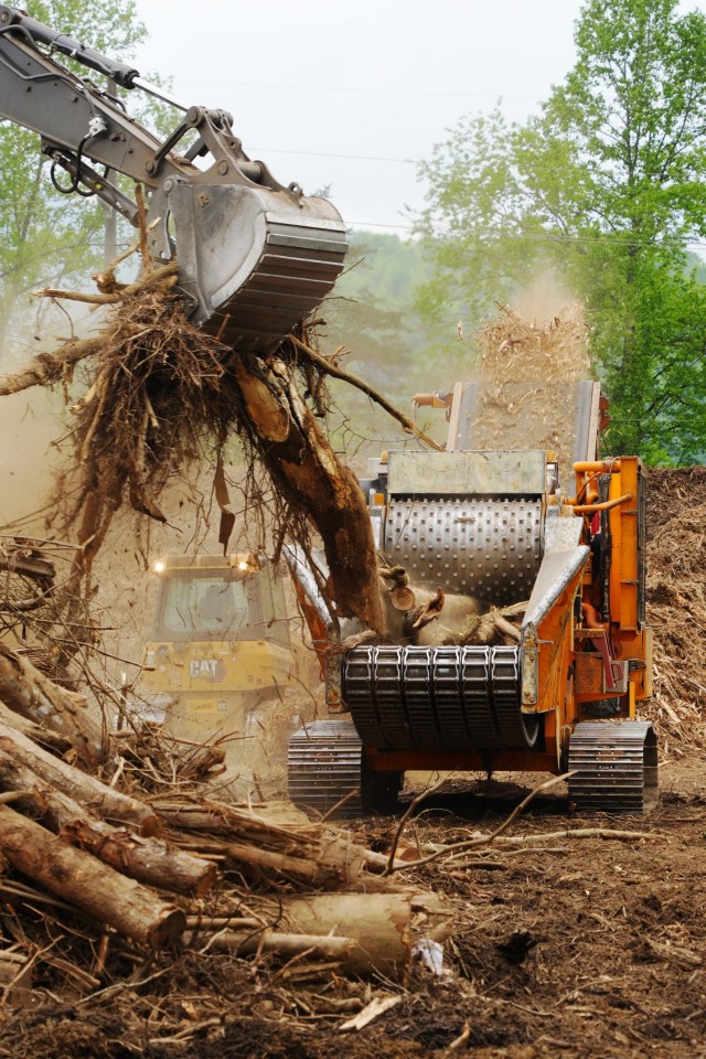 An excavator loads vegetative debris into a grinder as mulch is expelled out at Old Fort temporary debris management site in Old Fort, North Carolina, April 24, 2025. The debris was gathered from waterways and private properties after Hurricane...