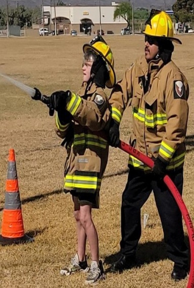 Boy Scout Lucas Estep holding a fire hose with the help of a firefighter.