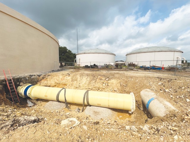 A giant water pipe sits in a recessed part of the ground, perpendicular to another pipe in use.