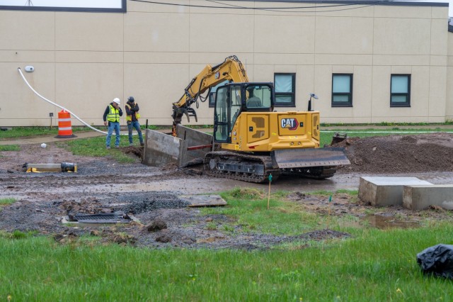 A work site - two people look down into a hole dug by an excavator.
