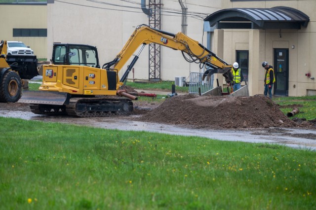 A work site - two people look down into a hole dug by an excavator.