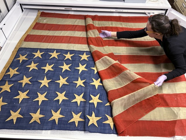 Museum Specialist Megan Hunter unfolds the 34-star flag in the museum's collection kept in flat storage April 17, 2025, at the Frontier Army Museum at Fort Leavenworth, Kansas. Photo by Stephanie Mahone/Fort Leavenworth Garrison Public Affairs Office