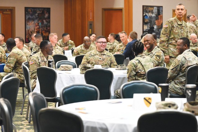Men and women sit around round tables in chairs in a large room.