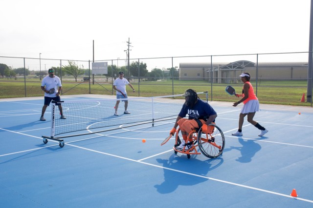 Cuatro personas están en la cancha de pickleball, los remar en la mano, dos personas a cada lado, y la pelota está rebotando.