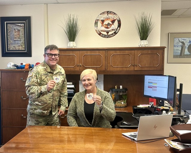 Colonel Rob Barnhill, the commander of the U.S. Army Electronic Proving Ground, or EPG, located at Fort Huachuca, Arizona, and his executive assistant, Allison Hadfield, hold up EPG emblems.