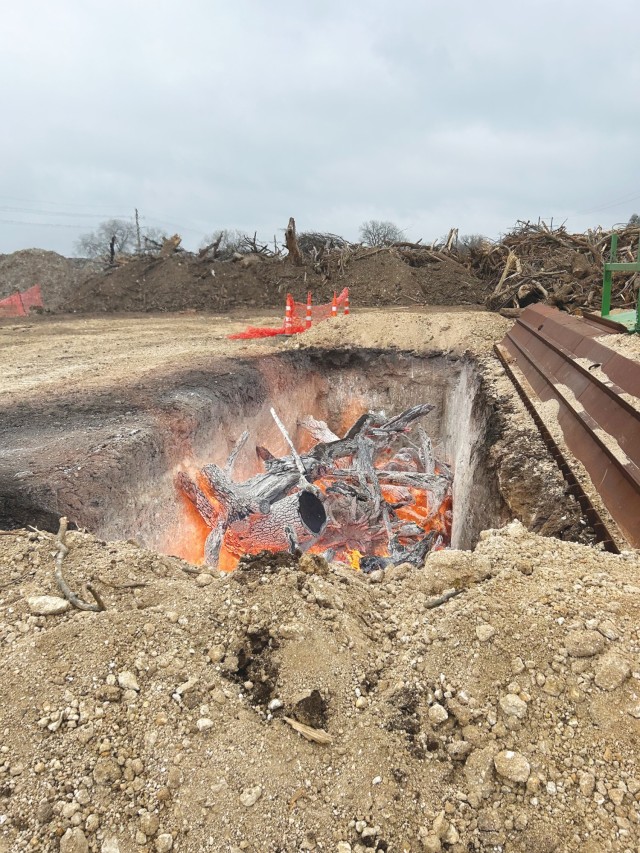 Parts of cut up trees sit in a fire in a recessed rectangular hole in the ground, glowing and white from being burnt.
