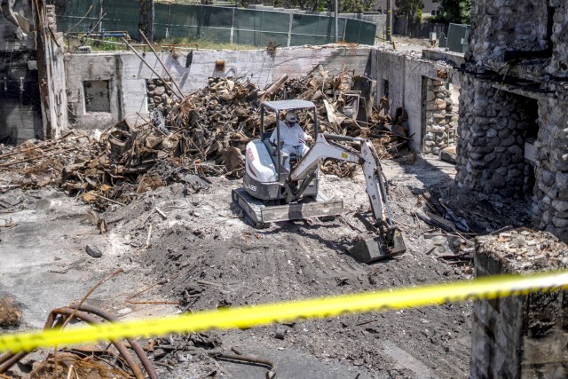 A contractor operates machinery to remove debris near the Davies Building at Farnsworth Park in Altadena, California, May 23, 2025. The structure is undergoing careful cleanup and partial preservation