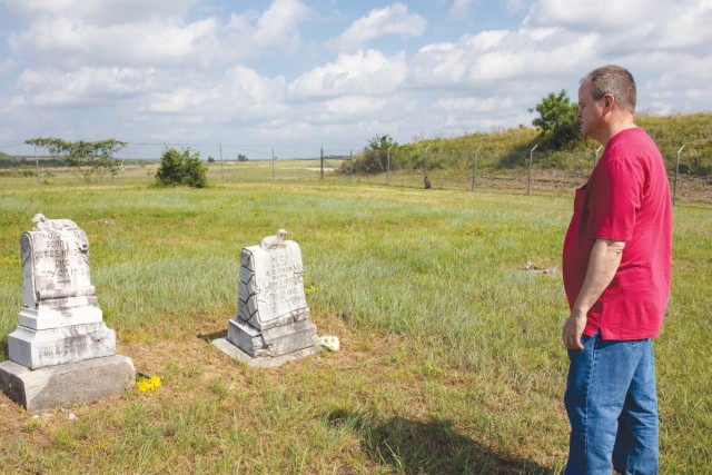 A man standing looks at two headstones in a field of grass.