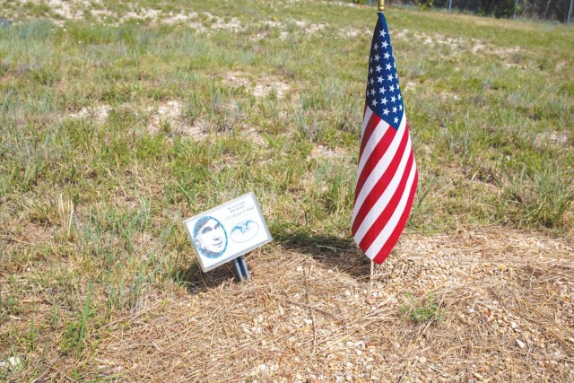 A small placard sits staked into the ground. To its left, a small American flag sits staked into the ground.