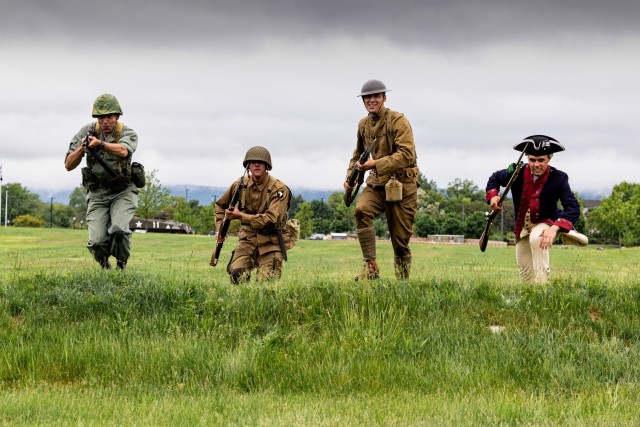 Four Soldiers from the Old Guard rush a hill while filming for the U.S. Army Intelligence and Security Command's Army 250 Birthday video. The soldiers are wearing uniforms from the Revolutionary War, World War I, World War II, and Vietnam War...