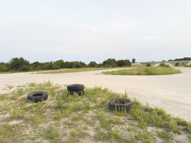 Four tires, two on top of another, lie on the ground next a large dirt road.