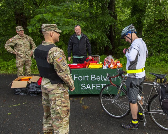 Col. David Stewart, center, and CSM Brandon Creel, left, welcome a rider who stopped at a water station for Bike to Work Day. The day continued with a large Safety, Health, Wellness and Resiliency Expo at the PX parking lot, to remind everyone of...