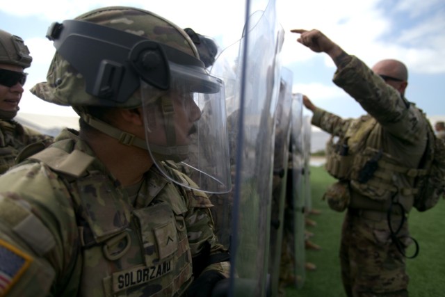U.S. Army Pvt. Arnoldo Solorzano, a cavalry scout with Troop A, 1st Squadron, 18th Cavalry Regiment, California Army National Guard, watches through his riot shield as U.S. Army Sgt. Jose Benitz, from the same unit, reviews proper positioning and...