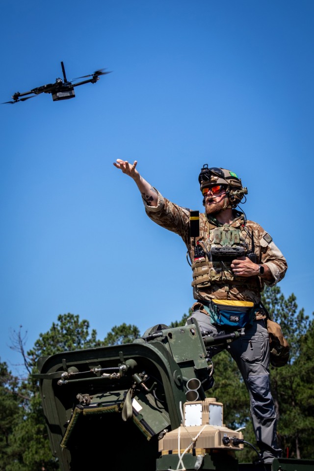 A technical expert stands by the hatch of a Stryker and releases a drone to fly over a suspected mine field during a testing event.