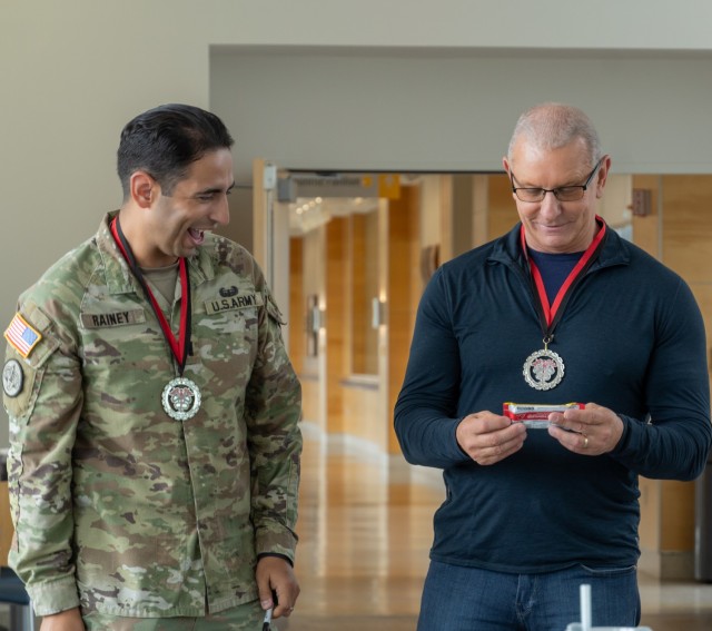 Army Cpt. Jams Rainey III, commander of Bravo Company, Medical Readiness Battalion, shares a laugh with Chef Robert Irvine after presenting him with the company’s signature Black Mambas coin.