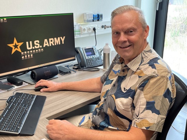 Jos Luijten sits at workplace desk with U.S. Army logo on desk computer screen