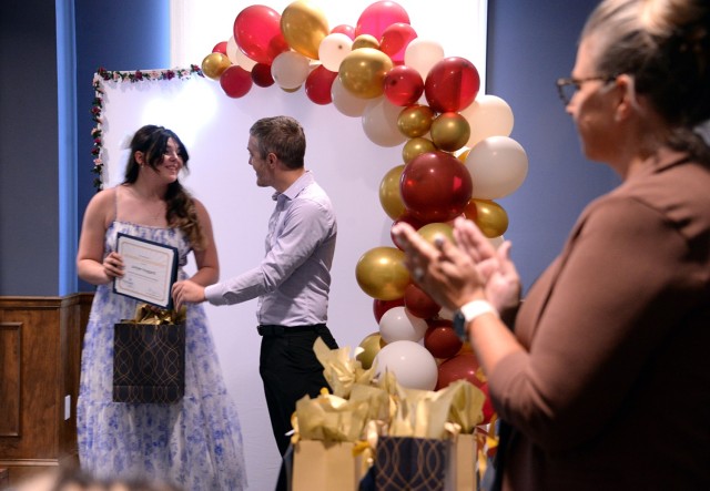 Scholarship recipient Juniper Huggard is presented a certificate and gift by Chase Cornett, The Michaels Organization senior investment manager, as Leigh Brown, Fort Leavenworth Frontier Heritage Communities assistant community director, applauds...