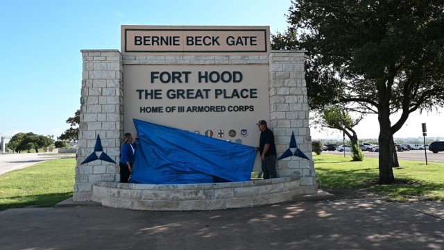 From left, Sohail Salgado, work reception technician, Fort Hood Directorate of Public Works, Operations and Maintenance Division, and Stephen Short, air-conditioning mechanic, DPW, OMD, drop a tarp at the Bernie Beck Gate sign to reveal the new...