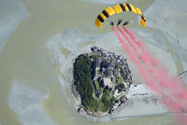 Sgt. 1st Class Rafael Torres, Sgt. 1st Class Zach Krietenstein, and Staff Sgt. Griffin Mueller of the U.S. Army Parachute Team fly in an advanced canopy maneuver for parachute jump at Mont Saint-Michel on 7 June 2024.  The parachute jump was part...