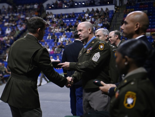 Command Sgt. Maj. Matthew O. Williams, Medal of Honor recipient, U.S. Army John F. Kennedy Special Warfare Center and School, presents a Green Beret to a student during a graduation ceremony and Regimental First Formation at the Crown Coliseum in...