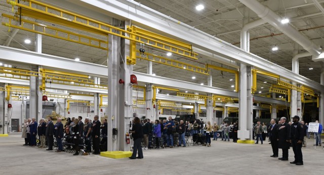 Attendees at a ribbon cutting ceremony for two updated military vehicle maintenance facilities at Red River Army Depot stand for the playing of the national anthem.
