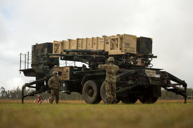 Two soldiers stand next to an MIM-104 Patriot system in a field.
