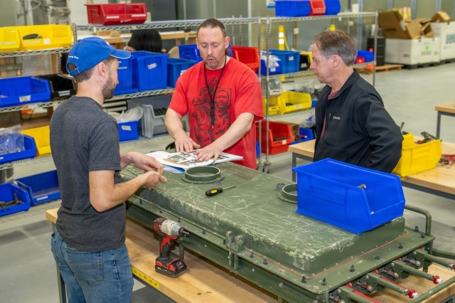 Tobyhanna proves commitment to quality with AS 9100 recertification/ three people stand in a work area - one speaks while two others look on