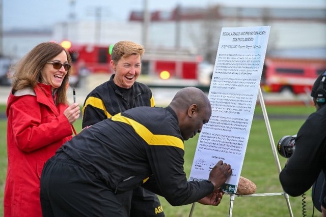 TACOM Sgt. Maj. Kofie B. Primus signs a commemorative copy of SAAPM proclamation as Chief Counsel Wendy Saigh (far left) and Commanding General Brig. Gen. Beth A. Behn look on.